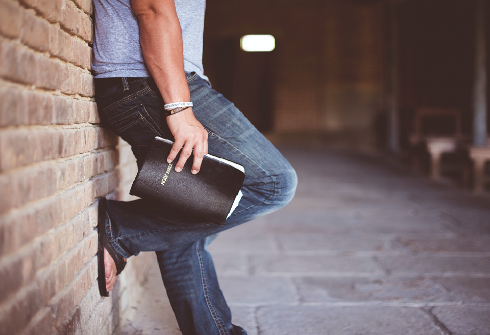 Man propped against brick wall with Bible in hand